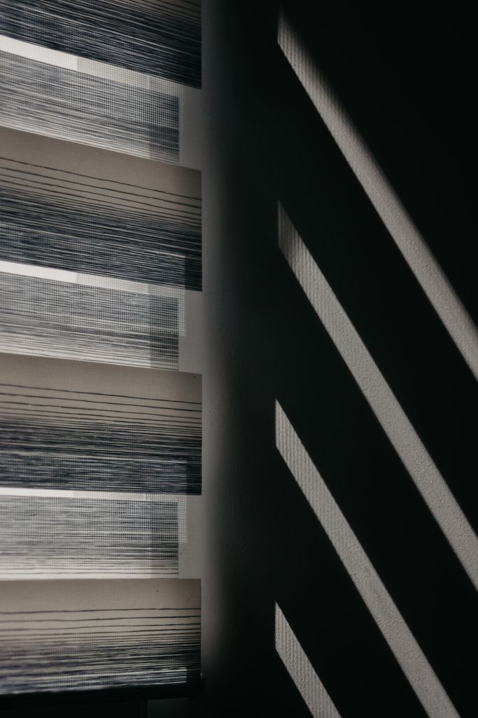Modern window blinds create striking shadows on a wall for an abstract visual effect.